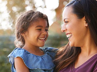 Smiling hispanic mother holding daughter laughing in garden at home, Kary Dental